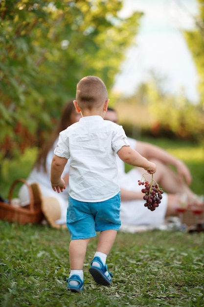 Um garotinho corre para seus pais e segura uvas nas mãos