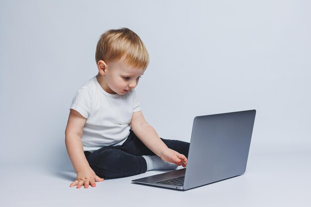 Um garotinho de 34 anos senta-se com um laptop em um fundo branco Uma criança em uma camiseta branca e calça preta olha para um laptop Crianças modernas