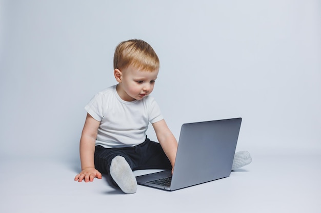 Um garotinho de 34 anos senta-se com um laptop em um fundo branco Uma criança em uma camiseta branca e calça preta olha para um laptop Crianças modernas