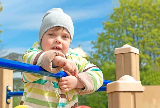 Um garotinho de casaco e chapéu no playground no parque