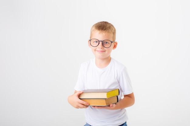 Um garotinho de óculos segurando uma pilha de livros em um fundo branco isolado
