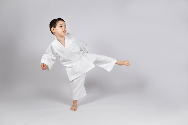 Um garotinho de quimono pratica karatê em um fundo branco