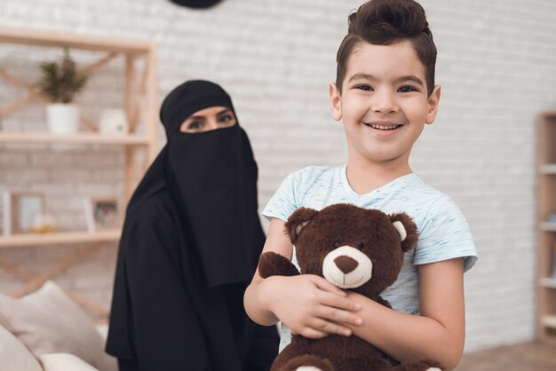 Um garotinho de uma família árabe está segurando um urso de brinquedo.