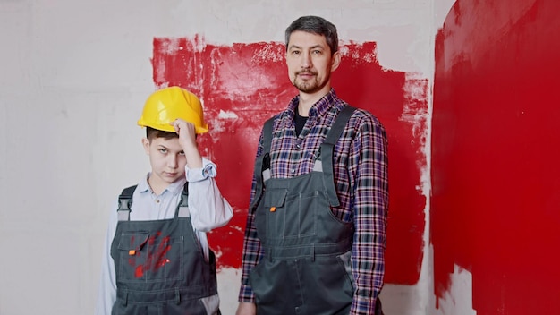 Um garotinho e seu pai pintando paredes um menino coloca um capacete e segurando um rolo