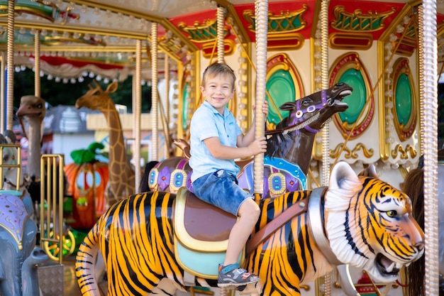 Um garotinho é uma criança loira em um parque de diversões, andando em um carrossel, sorrindo, regozijando-se