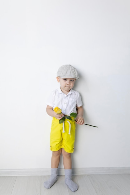 Um garotinho em estilo retrô com uma rosa amarela na mão fica perto de uma parede branca