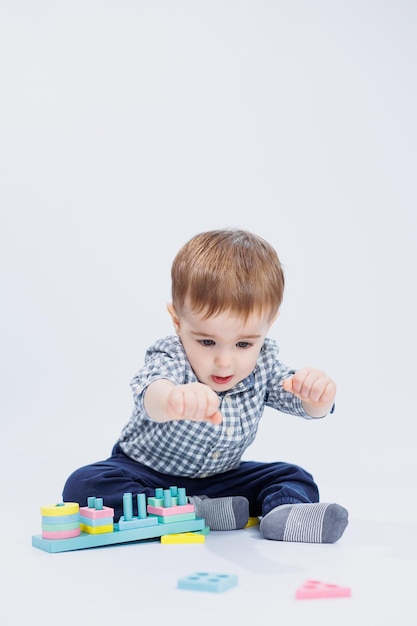 Um garotinho em uma camisa está construindo um brinquedo de madeira colorido em um fundo branco o conceito de jogos de desenvolvimento infantil para brinquedos infantis copiar espaço