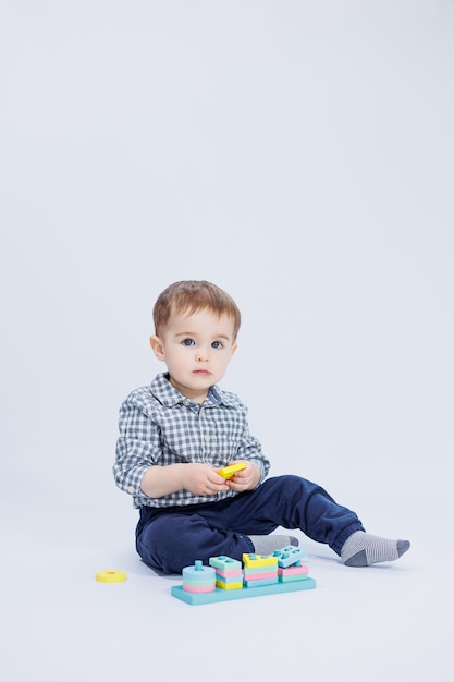 Um garotinho em uma camisa está construindo um brinquedo de madeira colorido em um fundo branco O conceito de jogos de desenvolvimento infantil para brinquedos infantis Copiar espaço