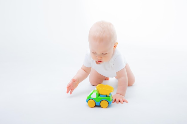 um garotinho em uma roupa branca brinca com um carro de brinquedo, sorrindo em um fundo branco