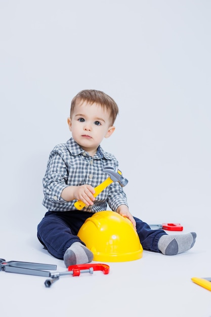 Um garotinho está brincando com um conjunto de ferramentas de construtor em um fundo branco Brinquedos de plástico para crianças