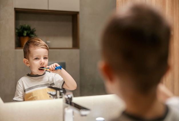 Um garotinho está escovando os dentes enquanto se olha no espelho