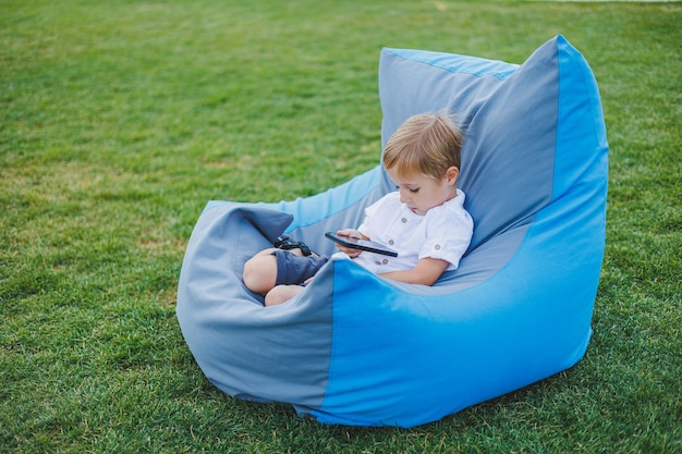 Um garotinho está sentado do lado de fora em um dia ensolarado e jogando no telefone