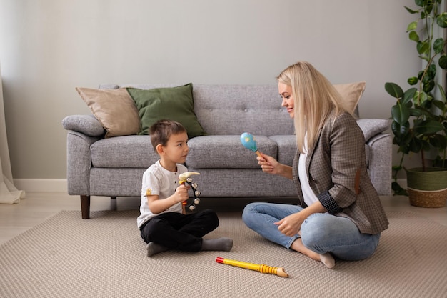 Um garotinho está sentado no chão com sua mãe e tocando instrumentos musicais