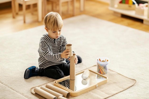 Um garotinho está sentado no chão e construindo uma torre enquanto brincava com um brinquedo montessori