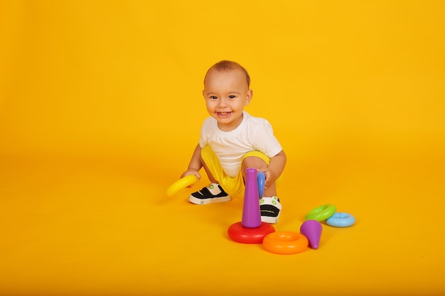 um garotinho feliz em uma camiseta branca e shorts amarelos joga um brinquedo de pirâmide
