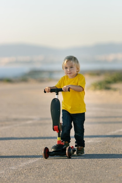 Um garotinho fica na estrada com uma scooter