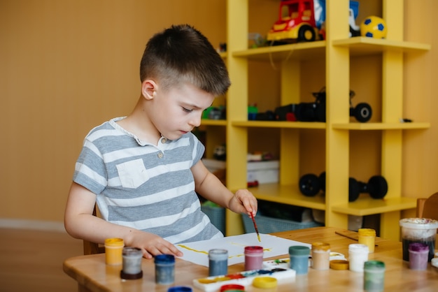 Um garotinho fofo está brincando e pintando em seu quarto