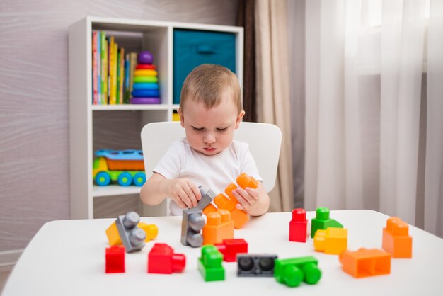 Um garotinho joga uma construção multicolorida colocada em uma mesa no quarto das crianças