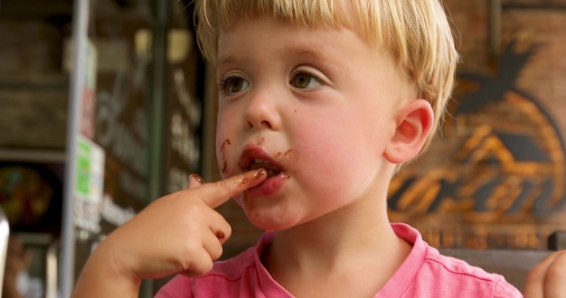 Um garotinho lambendo o chocolate de seus dedos depois de sorvete doce