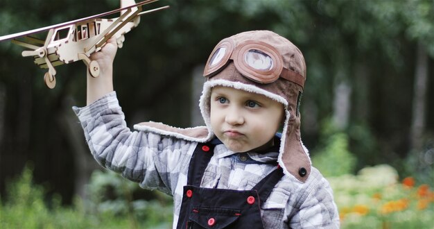 Um garotinho no capacete piloto de aviador de avião brinca com um avião de madeira a criança sonha voando