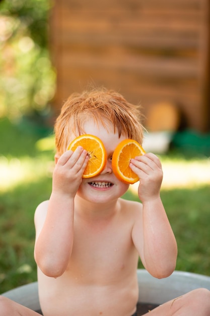 Um garotinho ruivo está brincando no banheiro com laranjas e sorrindoxDxA