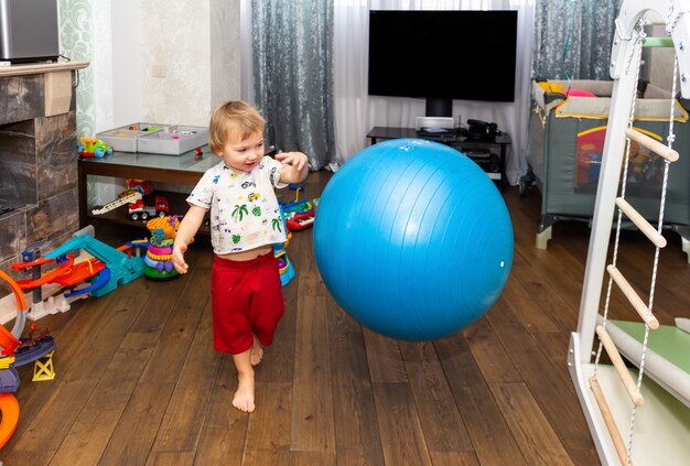 Um garotinho se diverte e brinca com uma grande bola de fitball azul na sala