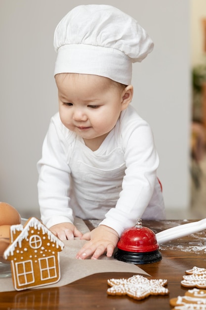 Um garoto asiático com chapéu e avental de chef cozinha biscoitos de gengibre de Natal na mesa da cozinha