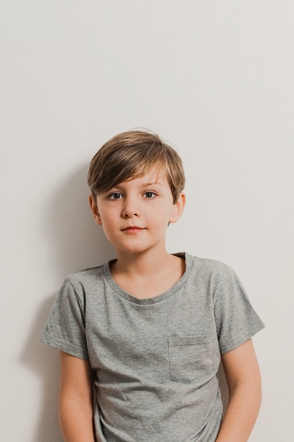 Um garoto bonito ao lado de parede branca, camisa cinza, sorrindo