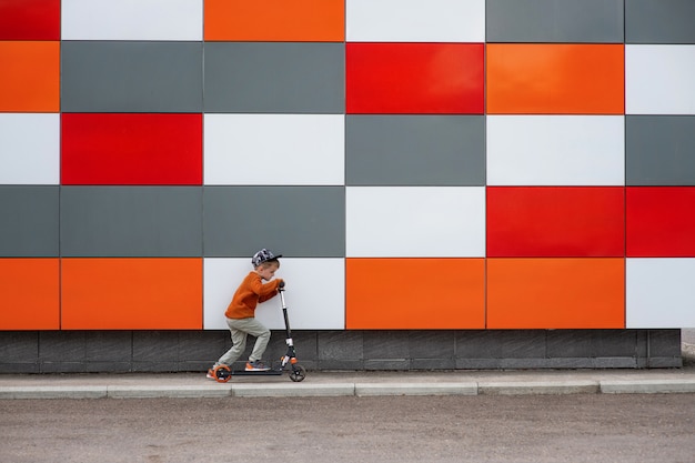 Um garoto de suéter laranja e calça jeans clara monta uma scooter