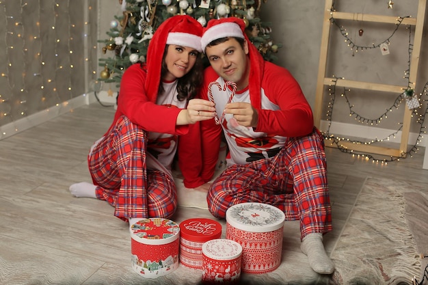um garoto e uma garota de pijama e um chapéu de Papai Noel estão sentados na árvore de Natal