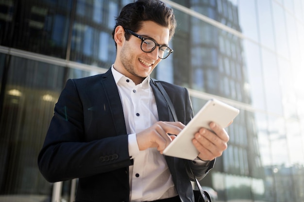 Um gerente de óculos um homem usa um tablet vai trabalhar no escritório em um terno de negócio