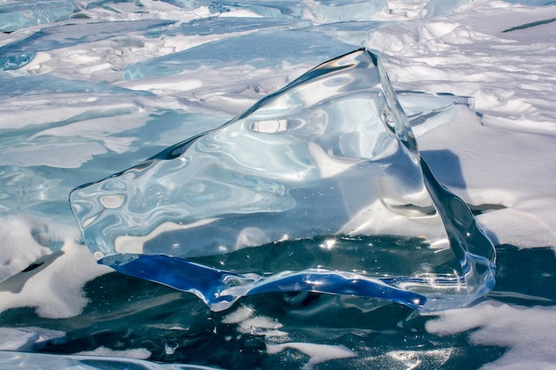 Um grande bloco de gelo derretido pelo sol fica no gelo do Lago Baikal com reflexos e distorções no gelo transparente