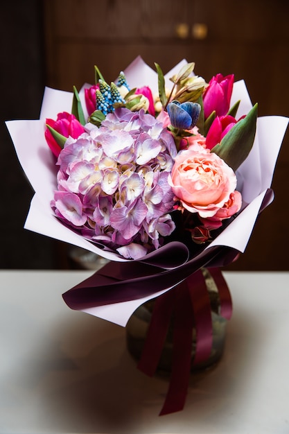 Um grande buquê de flores coloridas de vários tipos está em um vaso de vidro transparente.