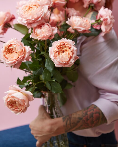 Um grande buquê de rosas frescas em um vaso de vidro contém uma estátua de menina em um fundo rosa