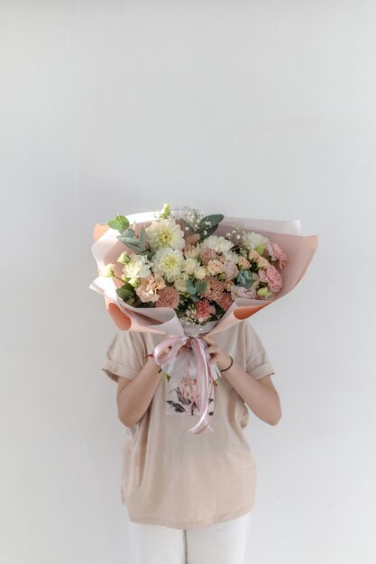 Um grande buquê delicado com dálias e rosas nas mãos de uma garota em um fundo branco