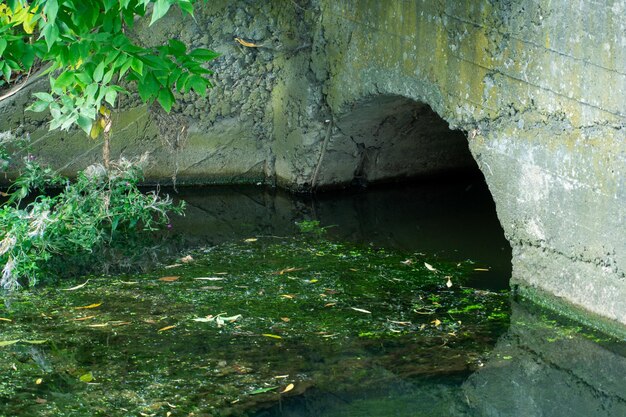 Um grande cano de concreto para desviar o rio sob a rodovia Água suja com vazamento de grandes canos de concreto Esgoto sujo do cano poluição ambiental Problema ambiental