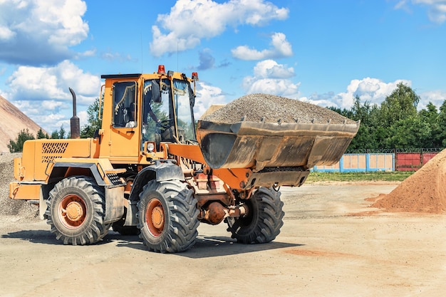 Um grande carregador frontal transporta brita ou cascalho em um balde em um canteiro de obras ou fábrica de concreto Transporte de materiais a granel Equipamento de construção Transporte de carga a granel