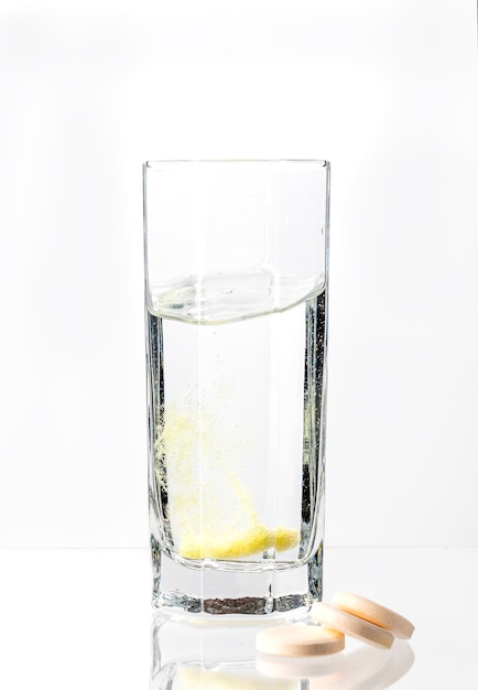 Um grande comprimido branco com dissolve-se em um copo de água em um fundo branco vitamina C