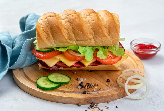 Um grande e delicioso sanduíche com ervas frescas, vegetais e linguiça em um fundo cinza