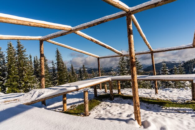 Um grande gazebo descoberto no topo da montanha fica em um prado branco coberto de neve banhado pela luz do sol frio e brilhante dos Cárpatos