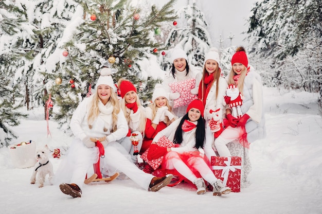 Foto um grande grupo de meninas com presentes de natal nas mãos, em pé na floresta de inverno. meninas com roupas vermelhas e brancas com presentes de natal na floresta de neve.