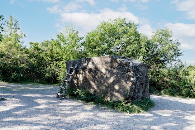 Um grande megalito de pedra enorme com uma escada contra o fundo de árvores verdes e um céu azul usado como plataforma de observação