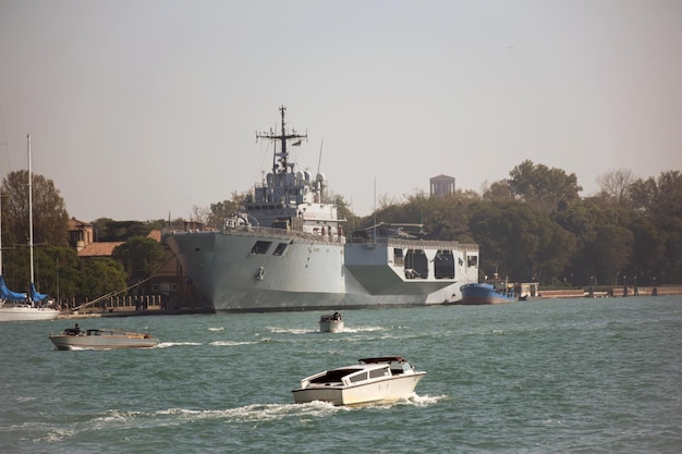 Um grande navio de guerra fica perto do cais no porto barcos de recreio flutuam em torno dele