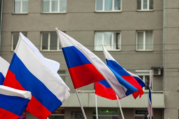 Um grande número de bandeiras russas em tricolor com listras de branco azul e vermelho contra o fundo das paredes de edifícios com janelas cinza durante um comício ou desfile