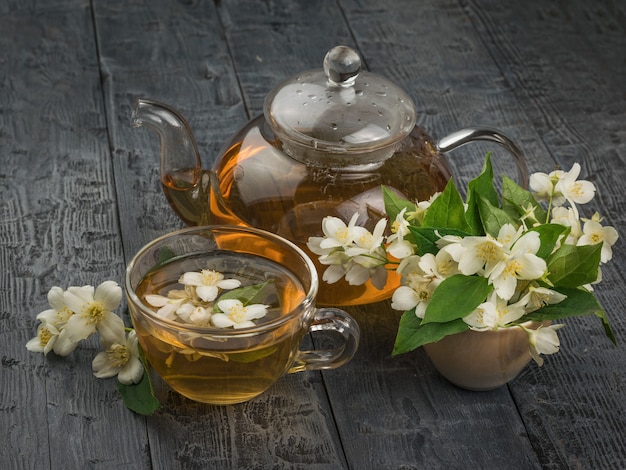 Um grande número de flores de jasmim e um bule de vidro com chá de flores sobre uma mesa de madeira.