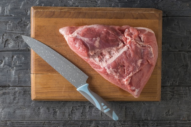 Um grande pedaço de carne de porco em uma placa de corte e uma grande faca em uma mesa de madeira. Ingredientes para cozinhar pratos de carne. A vista do topo.
