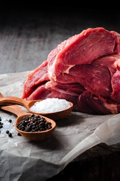 Um grande pedaço de carne de porco, sal e pimenta em colheres de pau em uma mesa de madeira