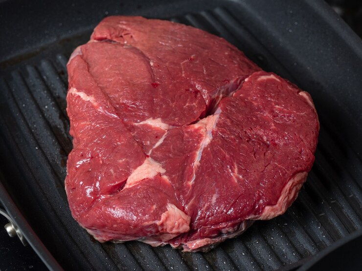 Um grande pedaço suculento de carne crua está na assadeira. Comida antes de cozinhar. A vista do topo.