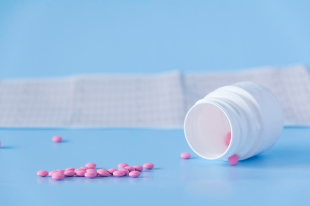 Um grande punhado de pílulas cor-de-rosa saiu de uma jarra branca em um eletrocardiograma do coração em um bl