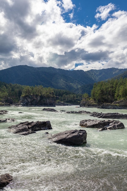 Um grande rio de montanha largo e cheio de fluxo rápido. Grandes rochas saem da água.